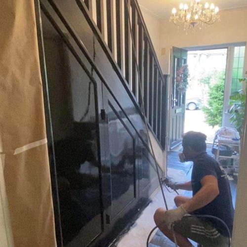 One of our KIAH Spraying decorators crouches as he sprays wooden stairs black.